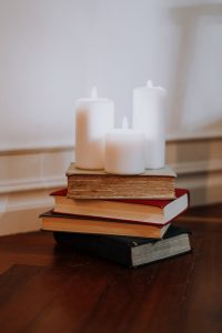 Stack of books with lit candles on a wooden surface, creating a cozy indoor atmosphere.