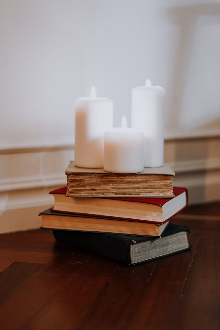 Stack of books with lit candles on a wooden surface, creating a cozy indoor atmosphere.